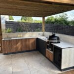 Cuisine d'extérieur Mado Prestige haut de gamme et sur mesure configuration en L finition tasseaux de bois avec évier plancha kamado et frigo tropicalisé