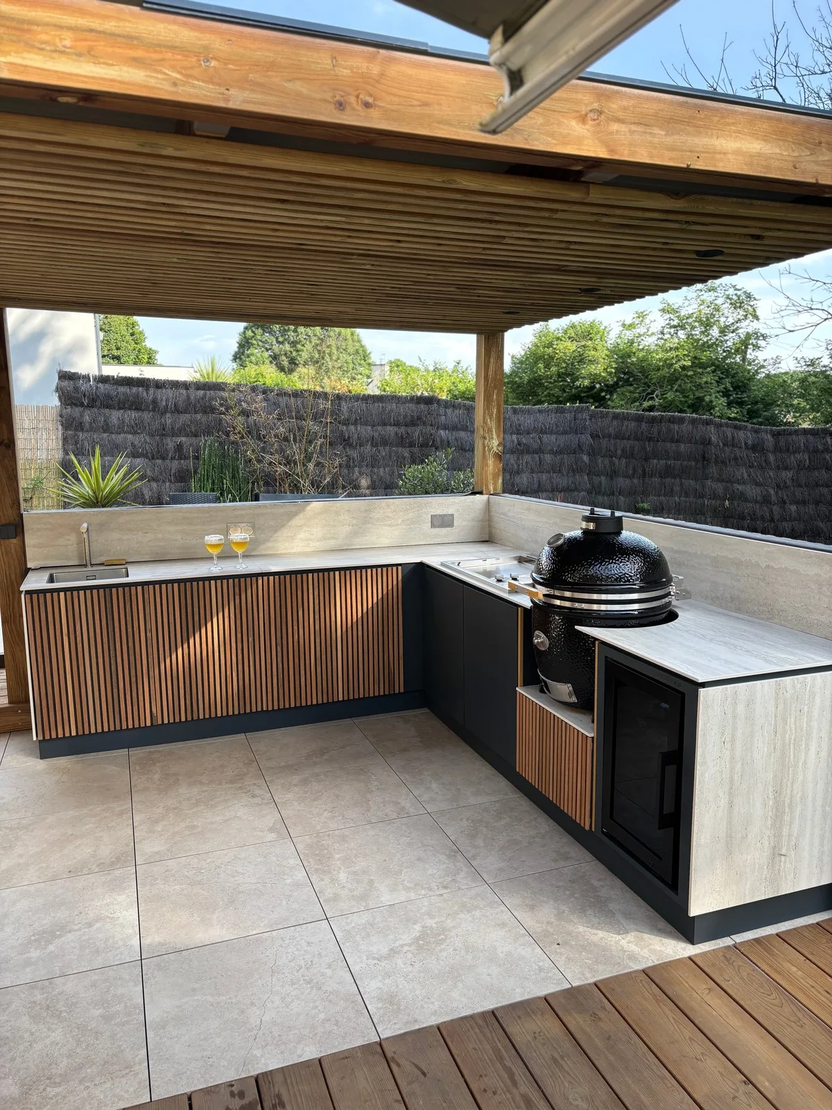 Cuisine d'extérieur Mado Prestige haut de gamme et sur mesure configuration en L finition tasseaux de bois avec évier plancha kamado et frigo tropicalisé